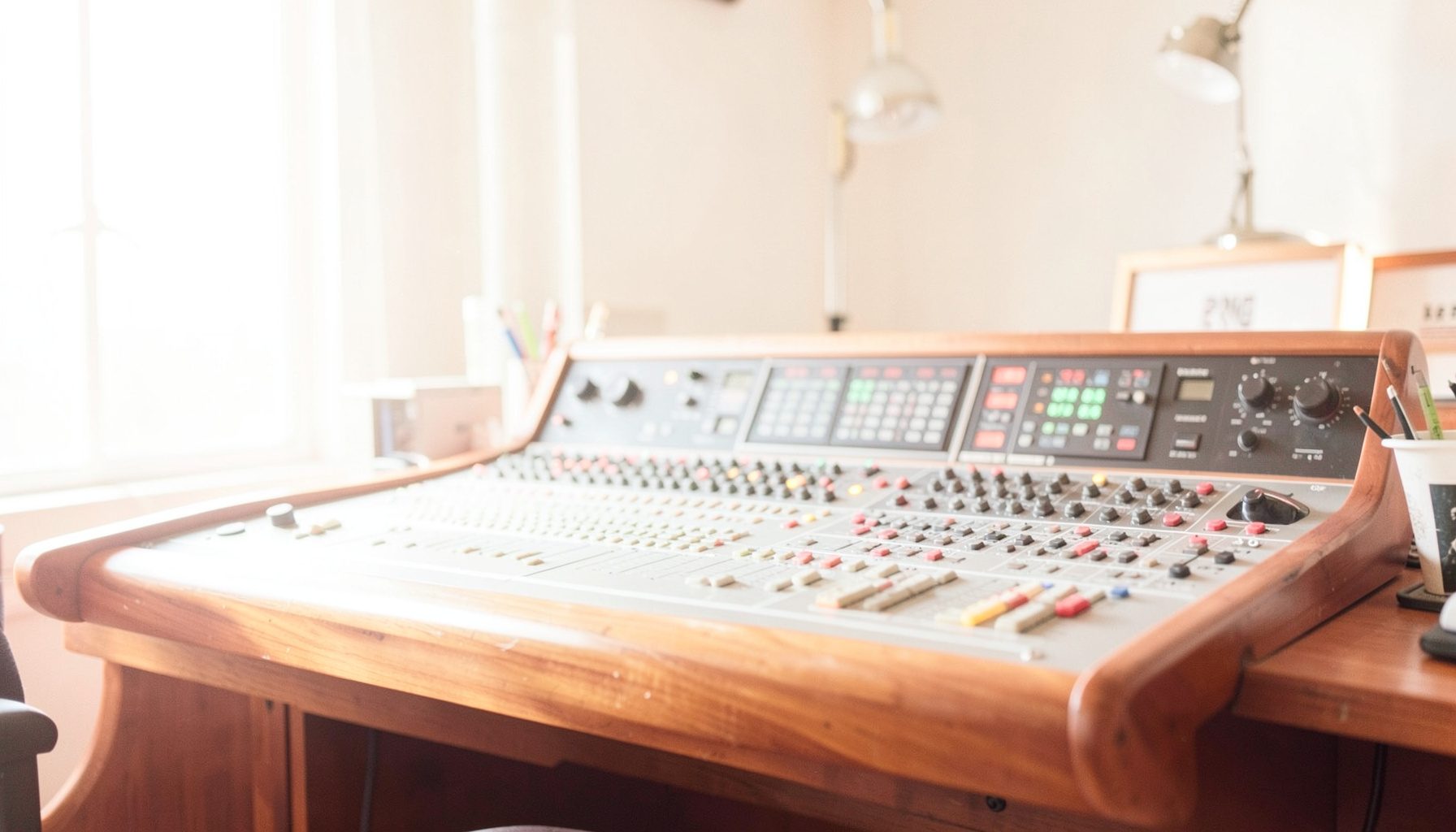 Bright, airy photograph of a sunlit recording studio console with warm wood tones and soft shadows, evoking a creative workspace
