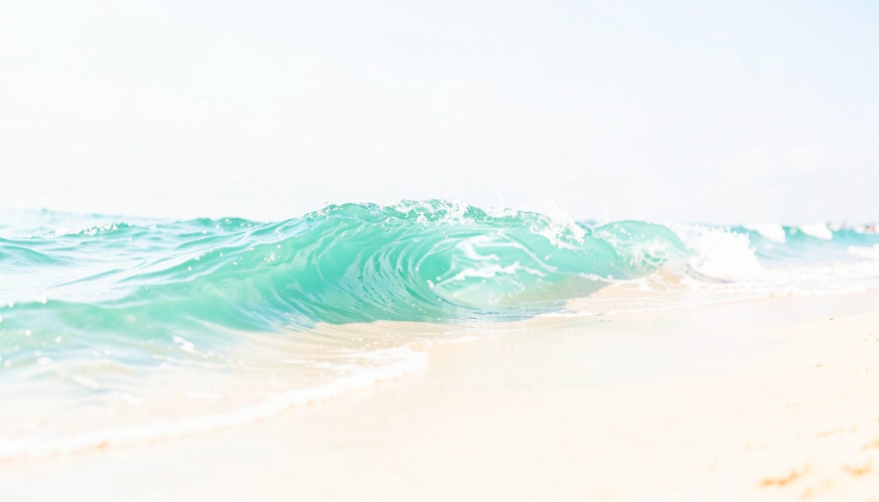 Small rectangular image of a bright turquoise ocean wave curling against a pale sandy shore under midday sun, suggesting energy and motion